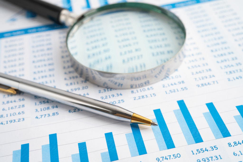 A magnifying glass pictured next to a ballpoint pen, on top of a printed balance sheet