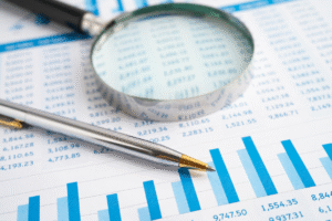 A magnifying glass pictured next to a ballpoint pen, on top of a printed balance sheet